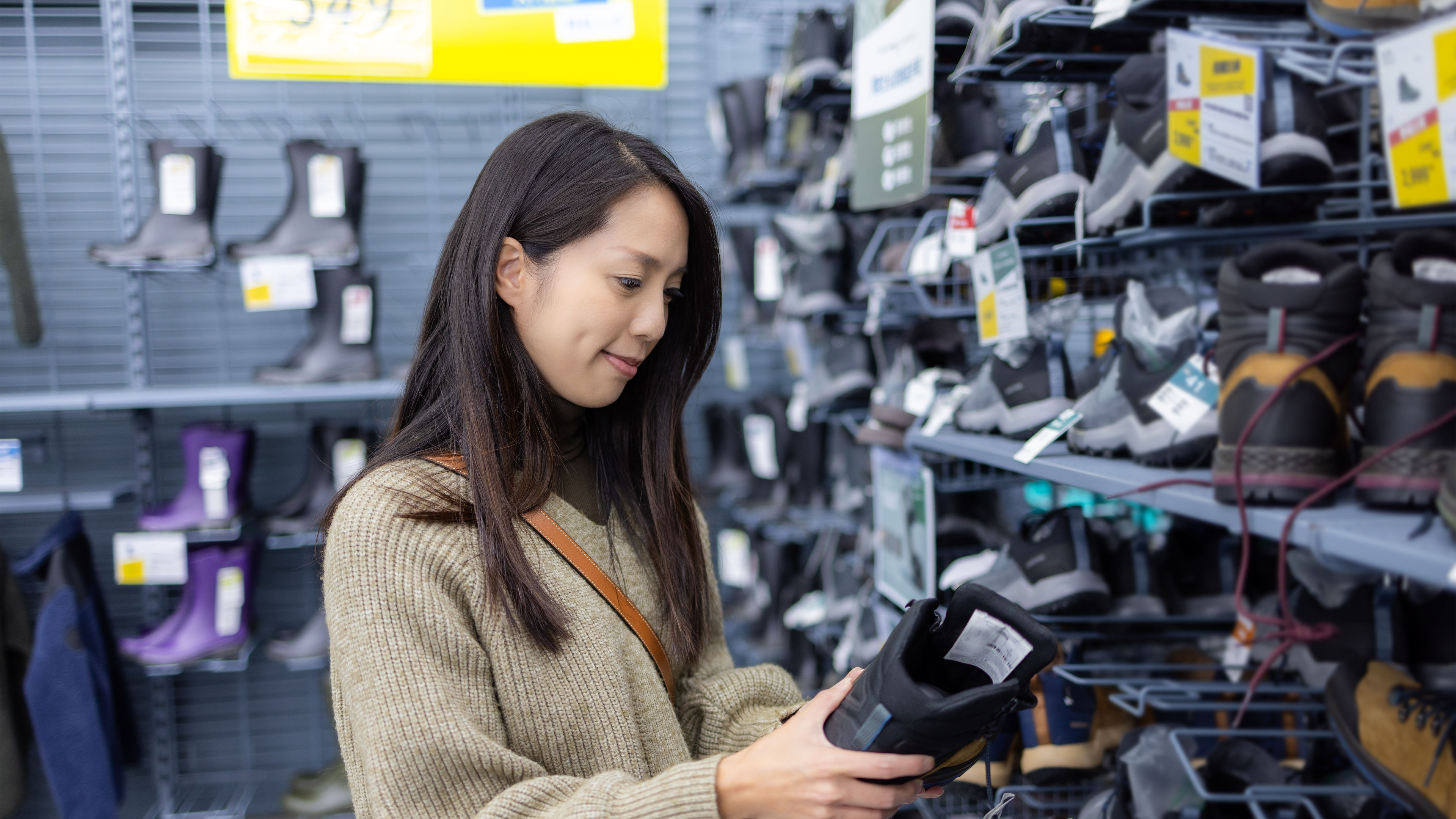 A woman choosing shoes from a shop with many shoes displayed on shelves, holding one pair in her hands.