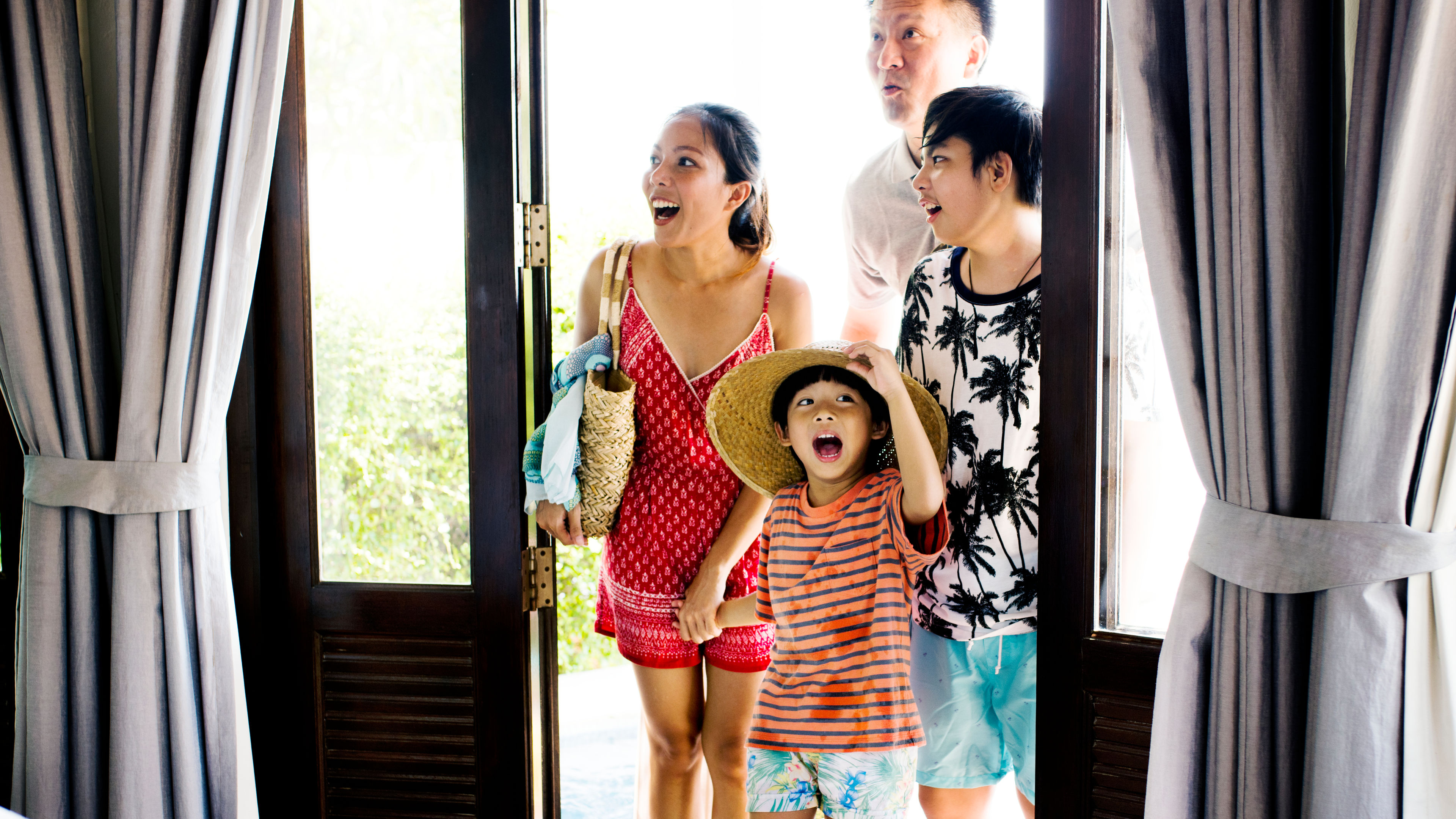 A couple and their two children happily entering a hotel room with smiles on their faces.