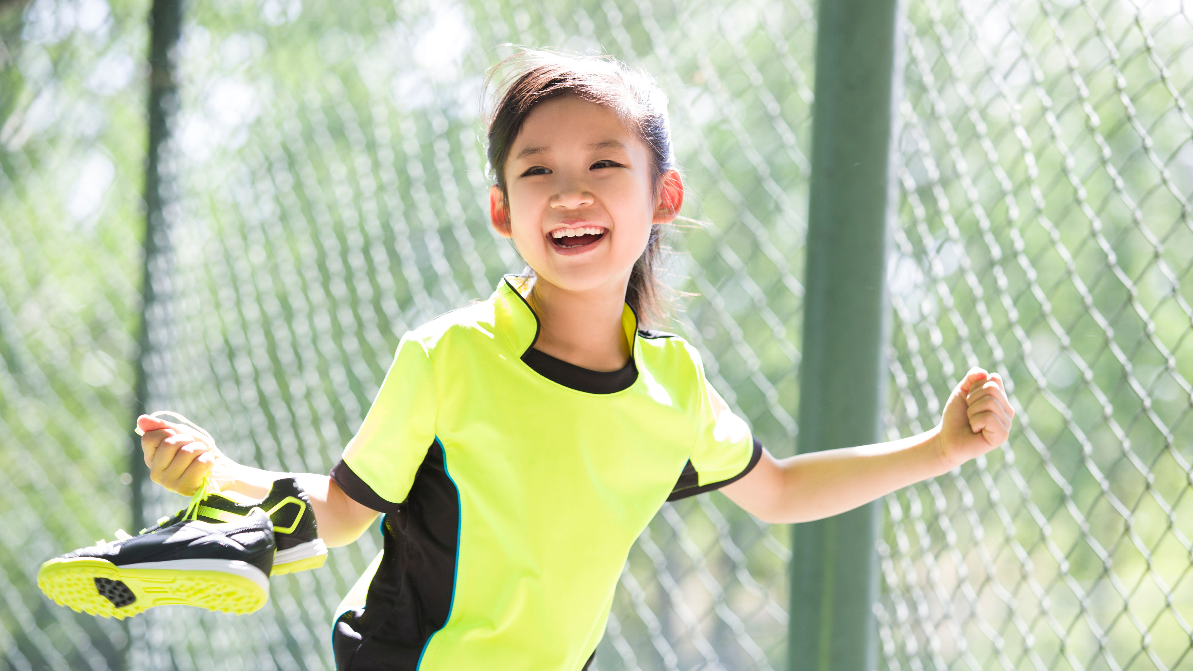 A happy girl wearing sportswear and smiling while holding a pair of athletic shoes in her hands.