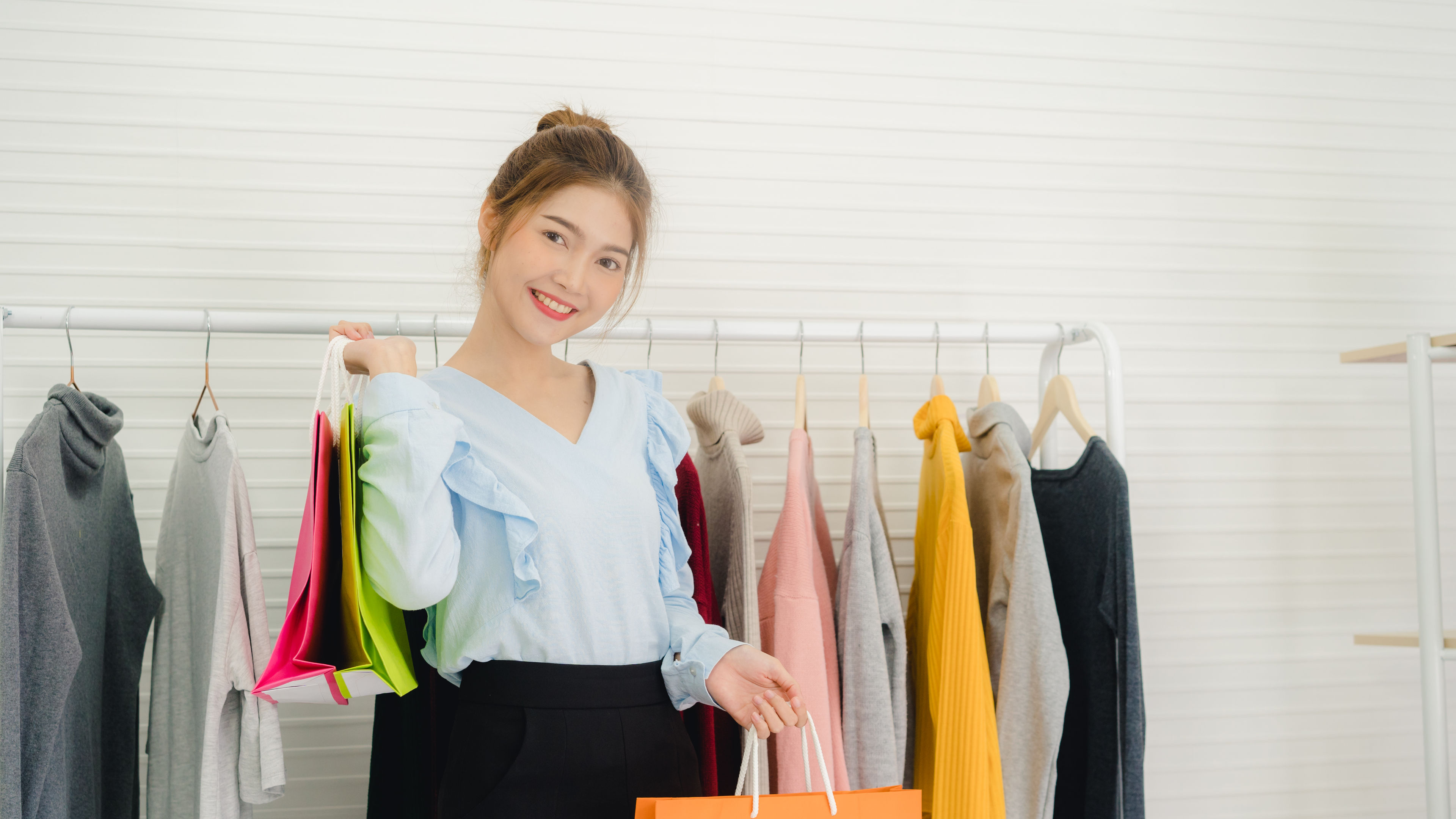 Asian woman with shopping bags Infront of rack of clothes.