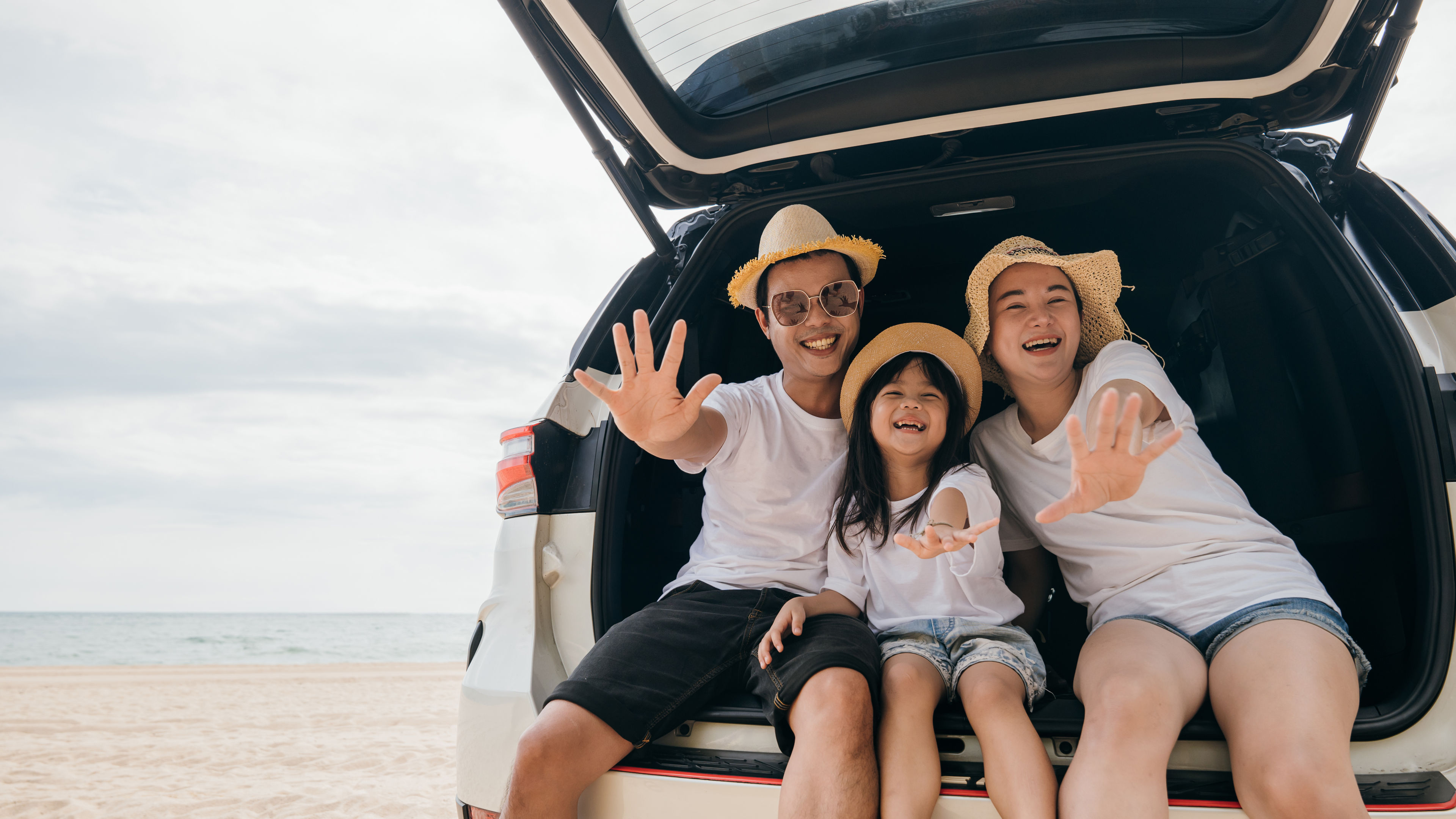 A cheerful family sits in the open trunk of their car on a beach 