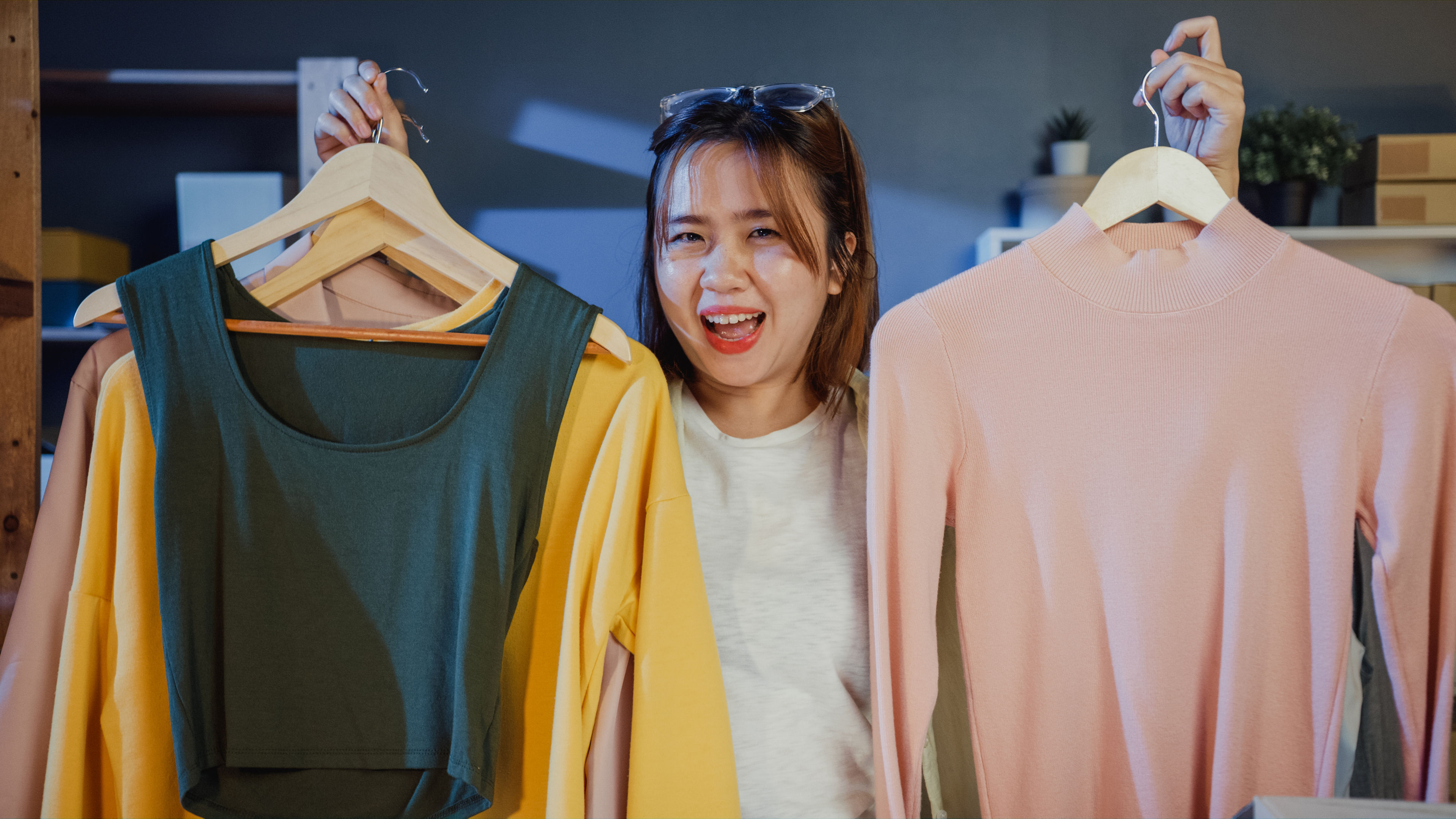 A smiling woman holds two colourful outfits. 

 