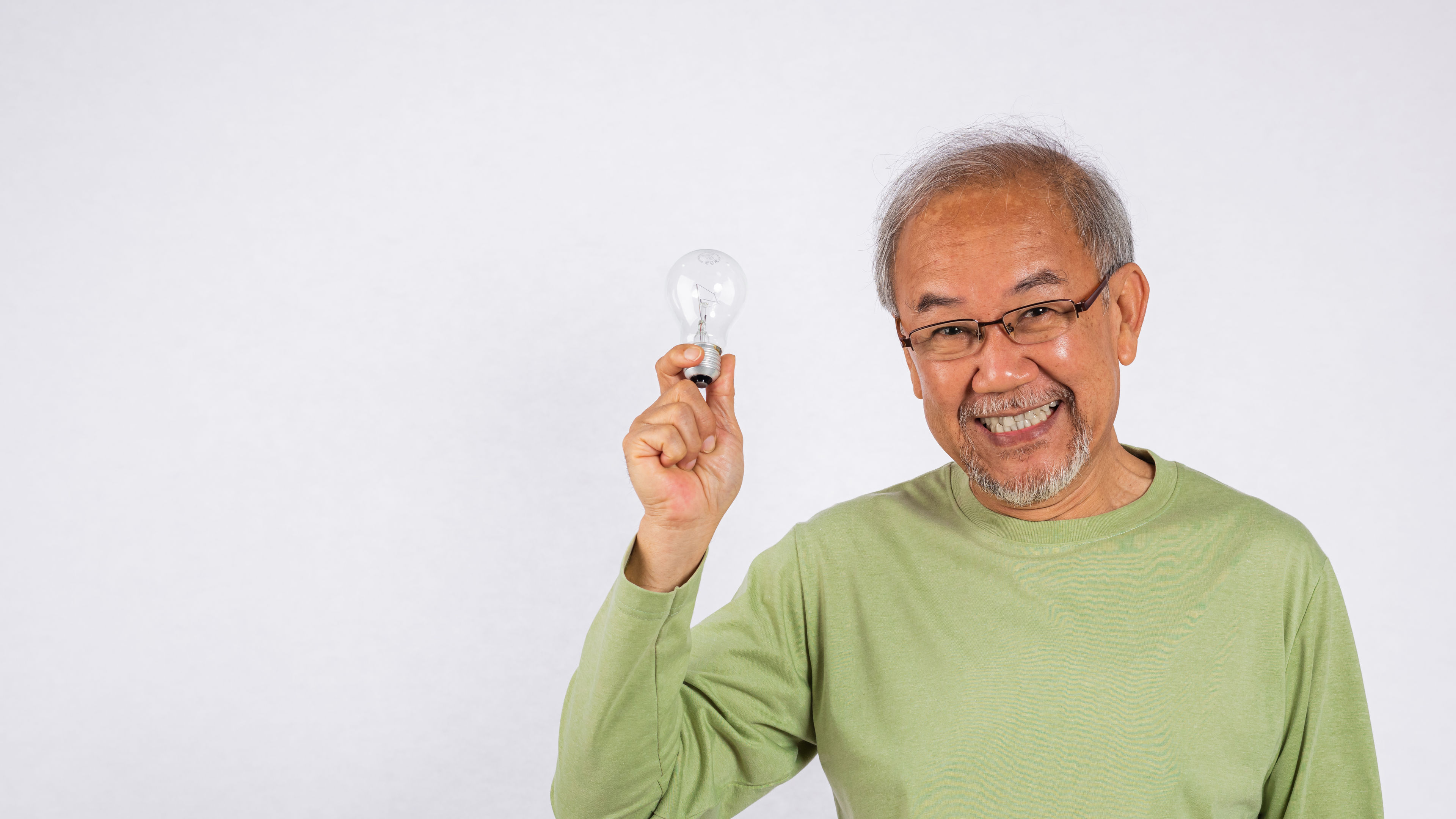 An elderly man smiles while holding a light bulb. 