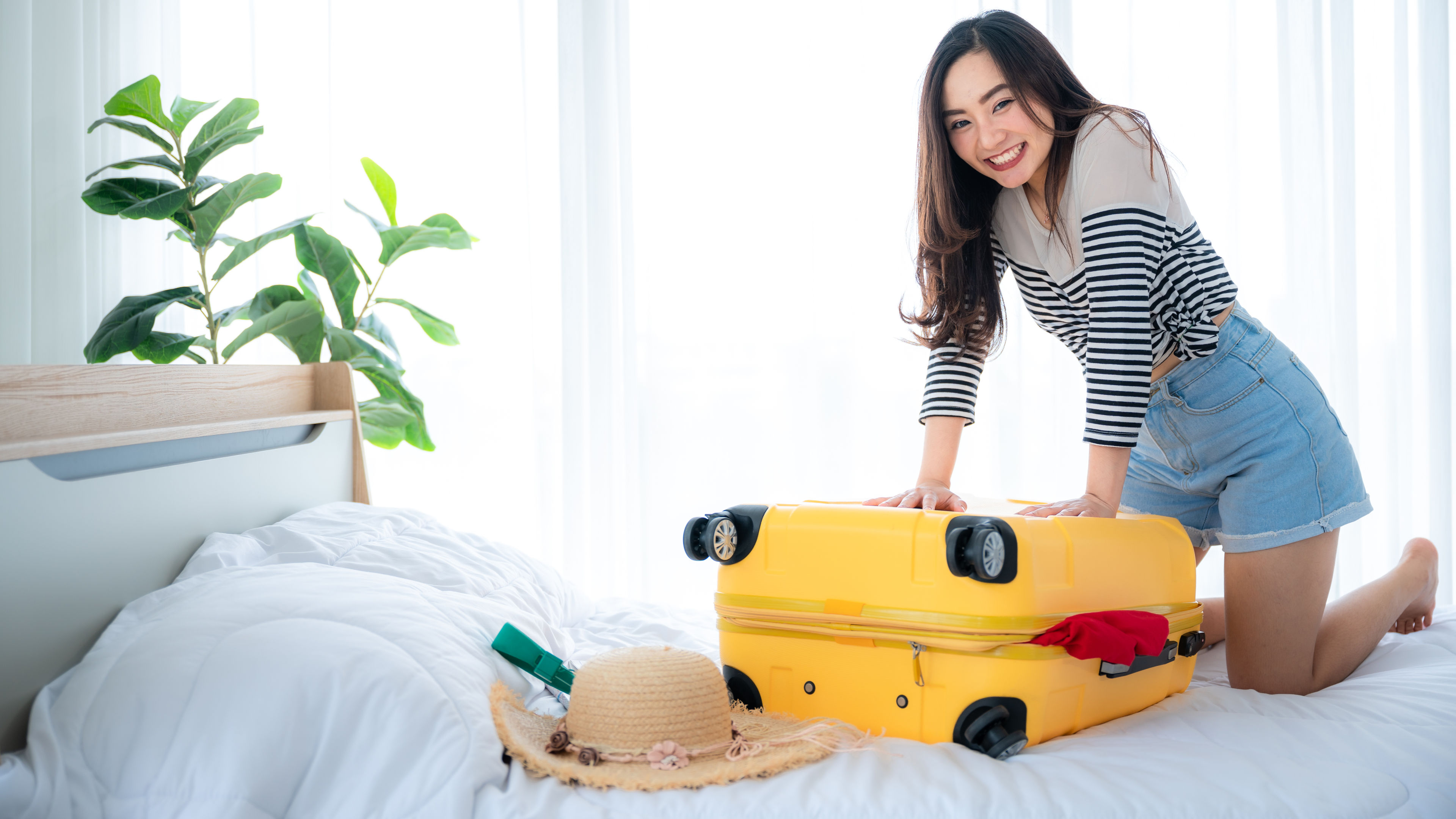 cheerful asian woman traveller with suitcase packed for a trip 