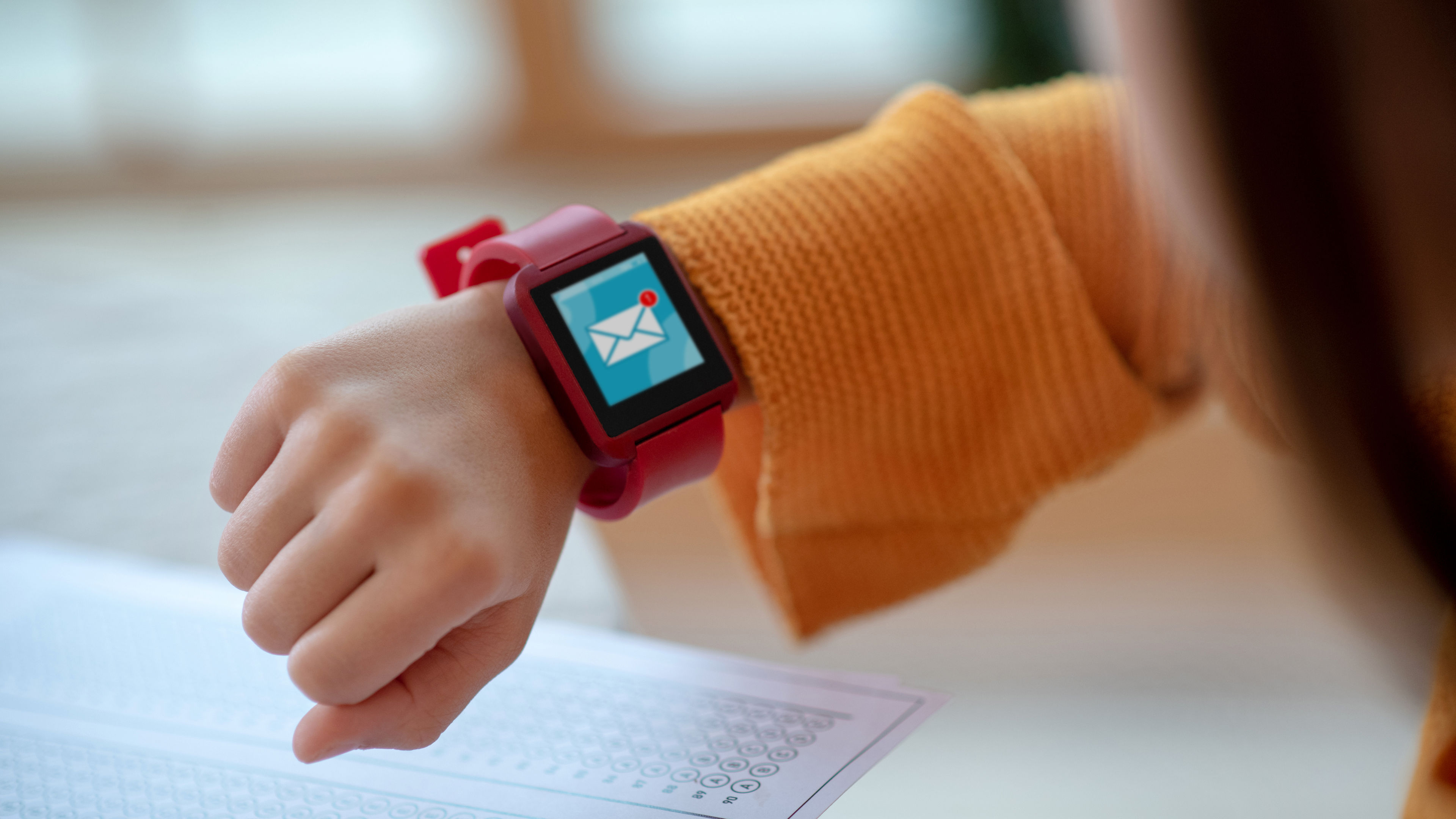 A girl’s wrist with a red smartwatch showing a notification. 