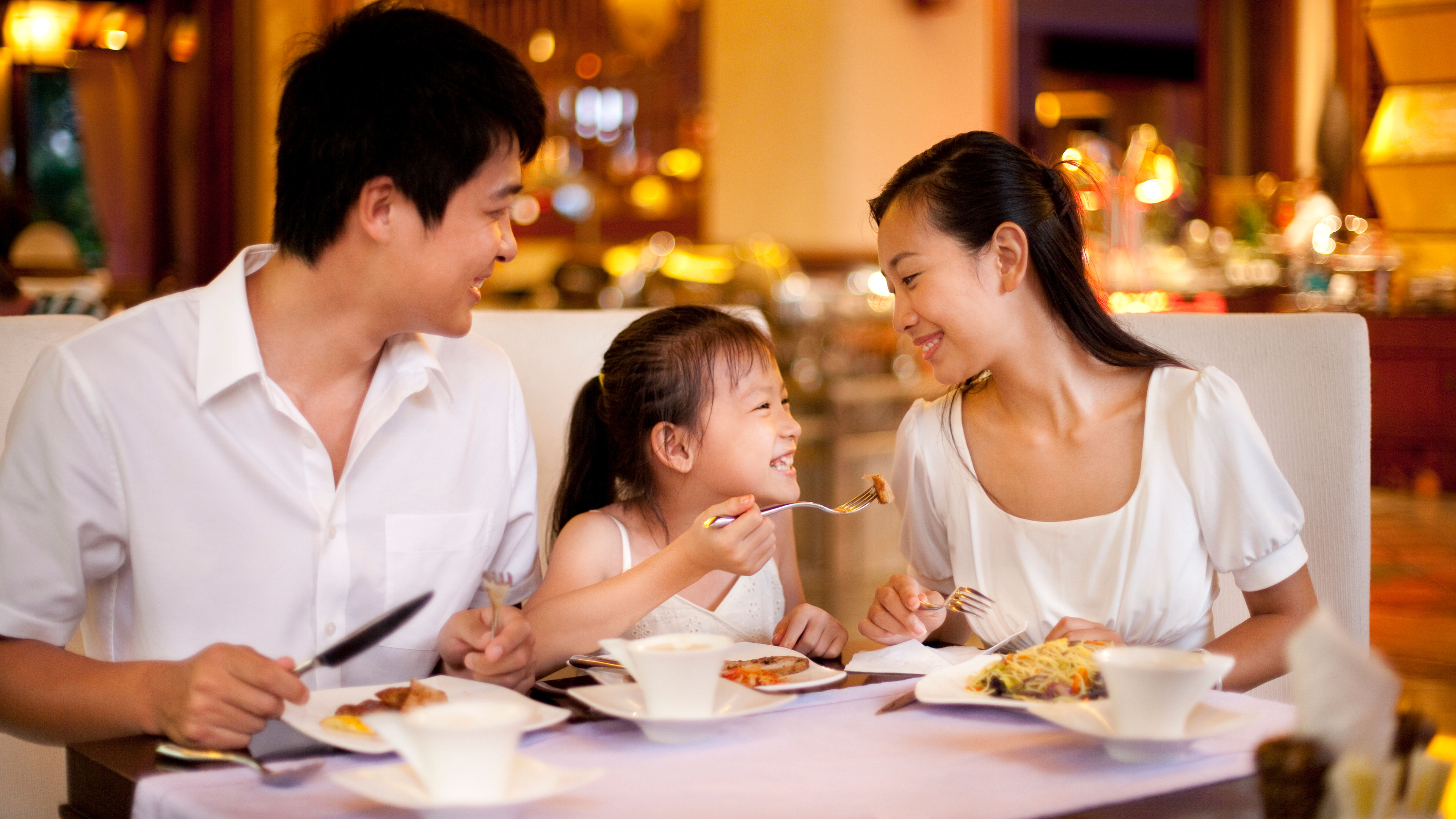 A family of three enjoying a meal together, with the parents and their child sitting around a dining table.  