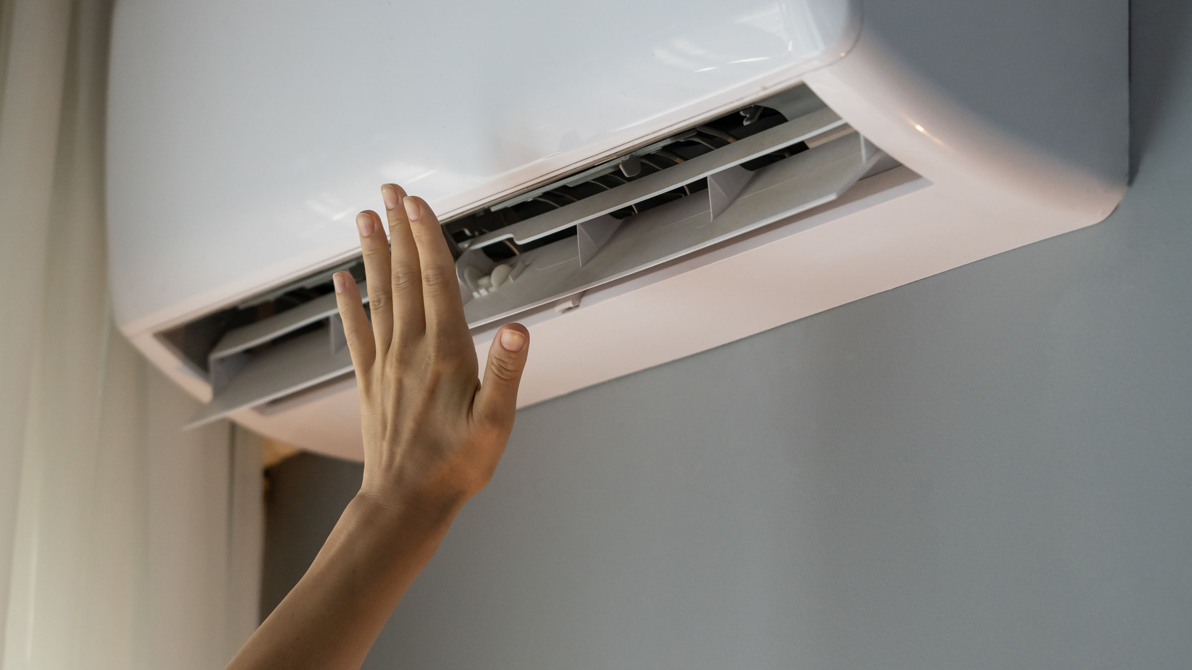 Hand extended toward an air conditioner, with cool air gently flowing out.  