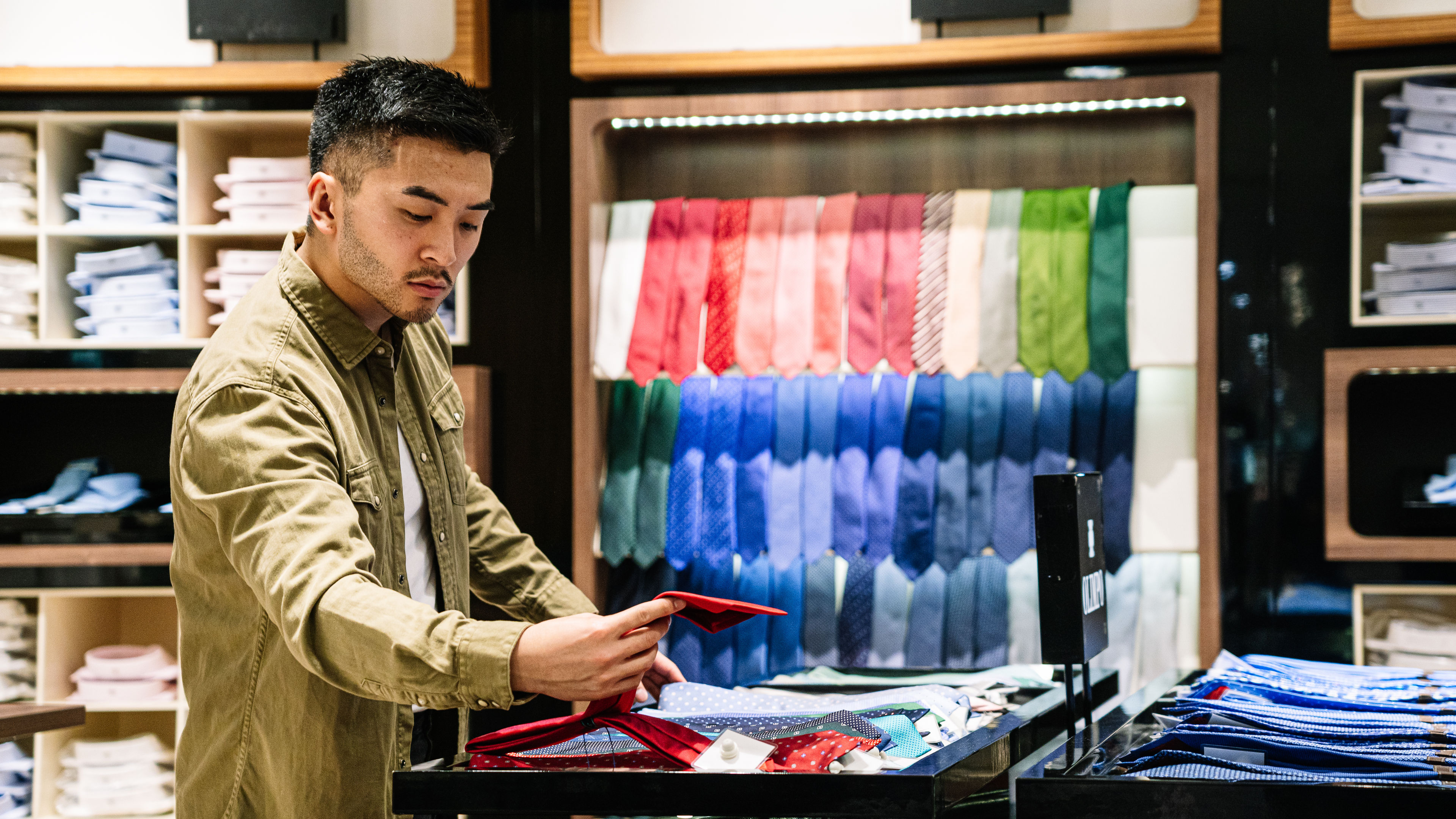 A man carefully selects neckties while browsing through options in a store. 