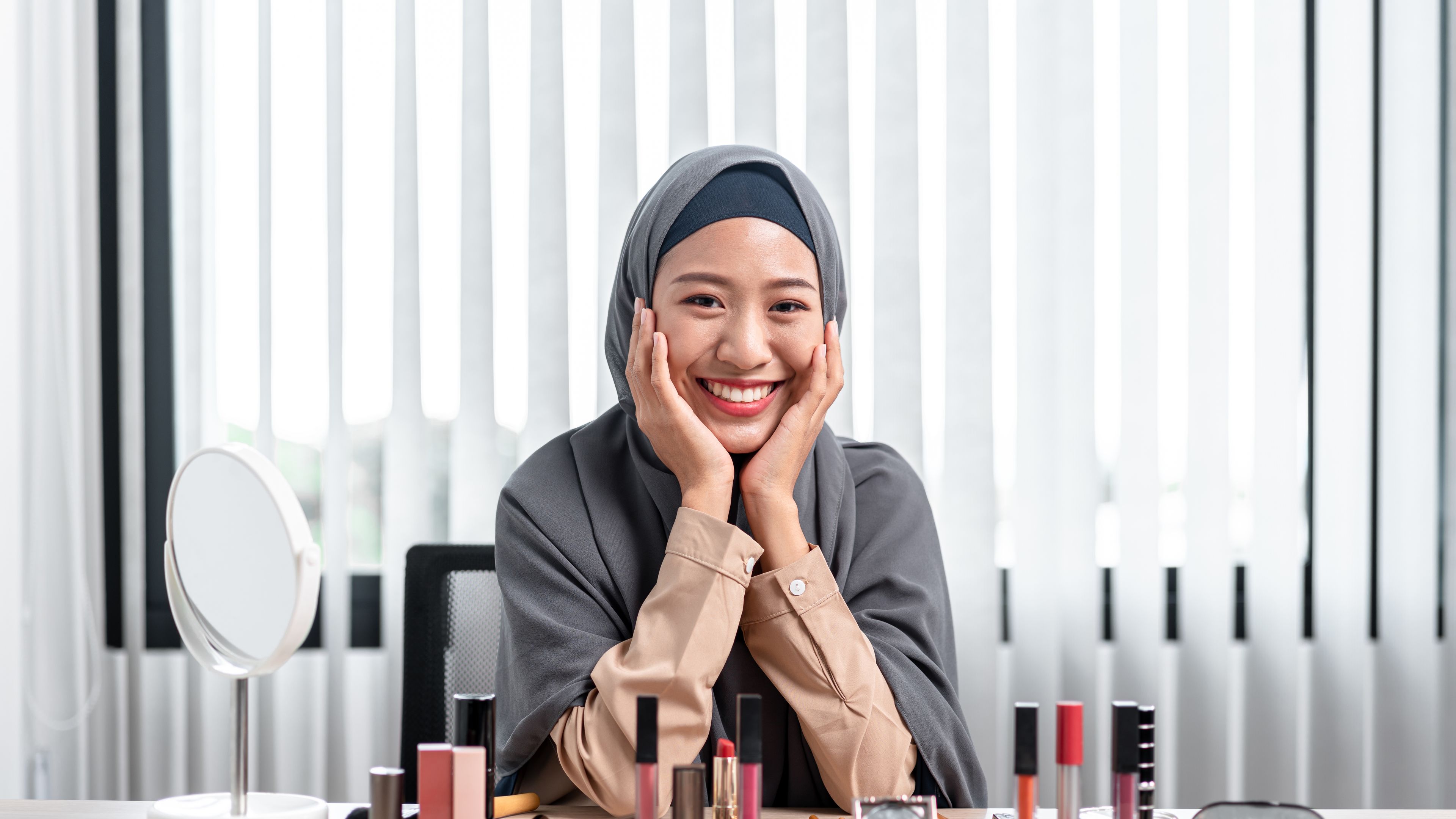 portrait of Asian Muslim woman looking at a camera and smiling while teaching a makeup tutorial online live 