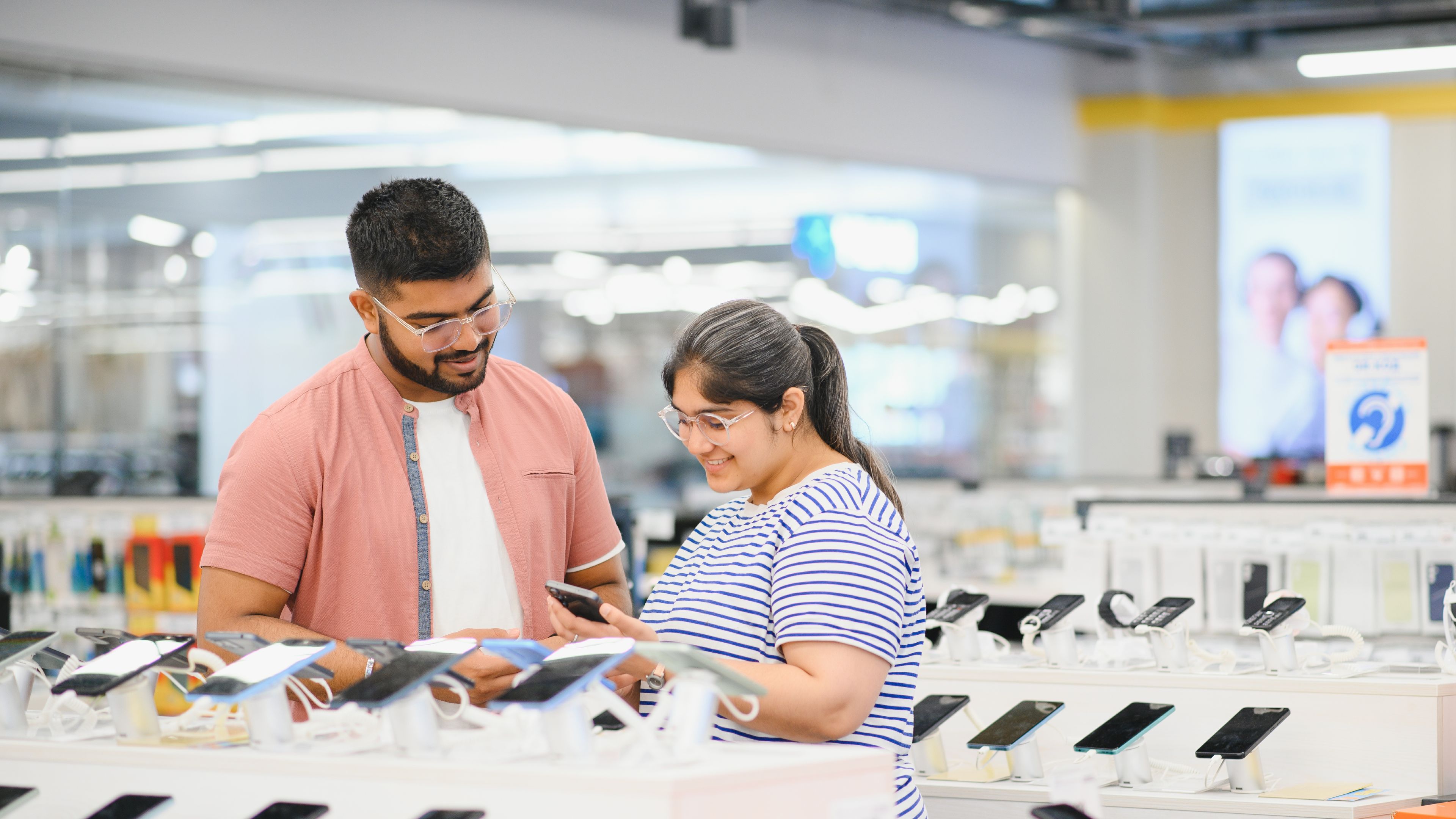 A couple explores an electronics store, excitedly purchasing the latest gadgets, from smartphones to smart home devices, as they enjoy discovering the newest tech innovations together. 