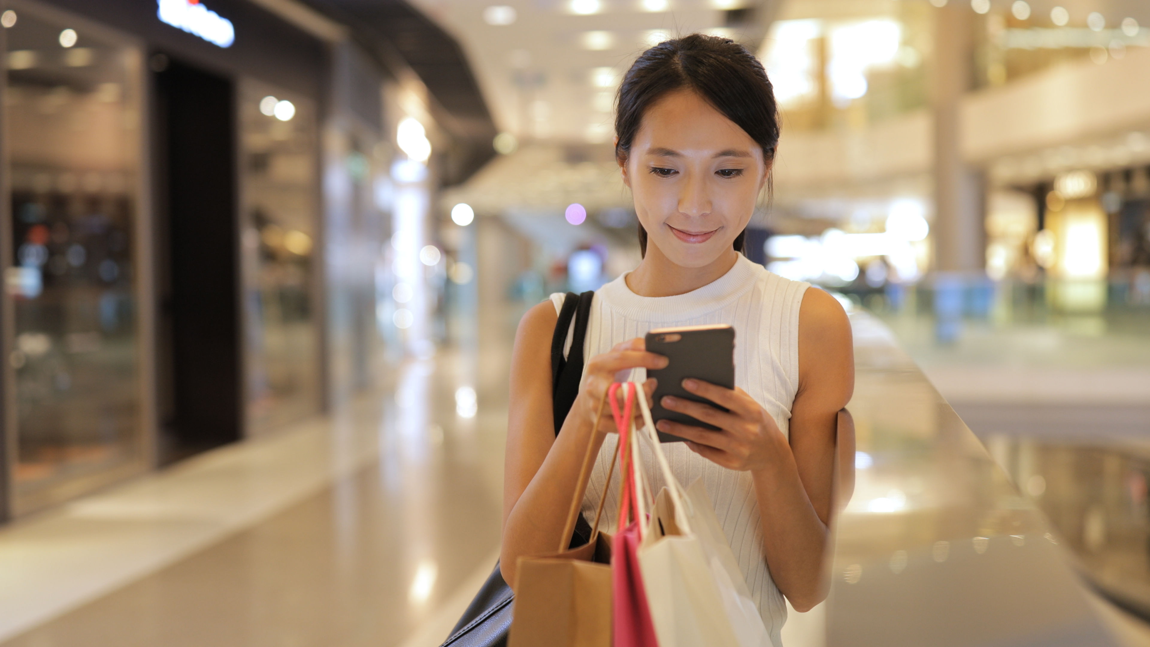 Woman shopping online with a smartphone while sitting on a couch, surrounded by shopping bags. 