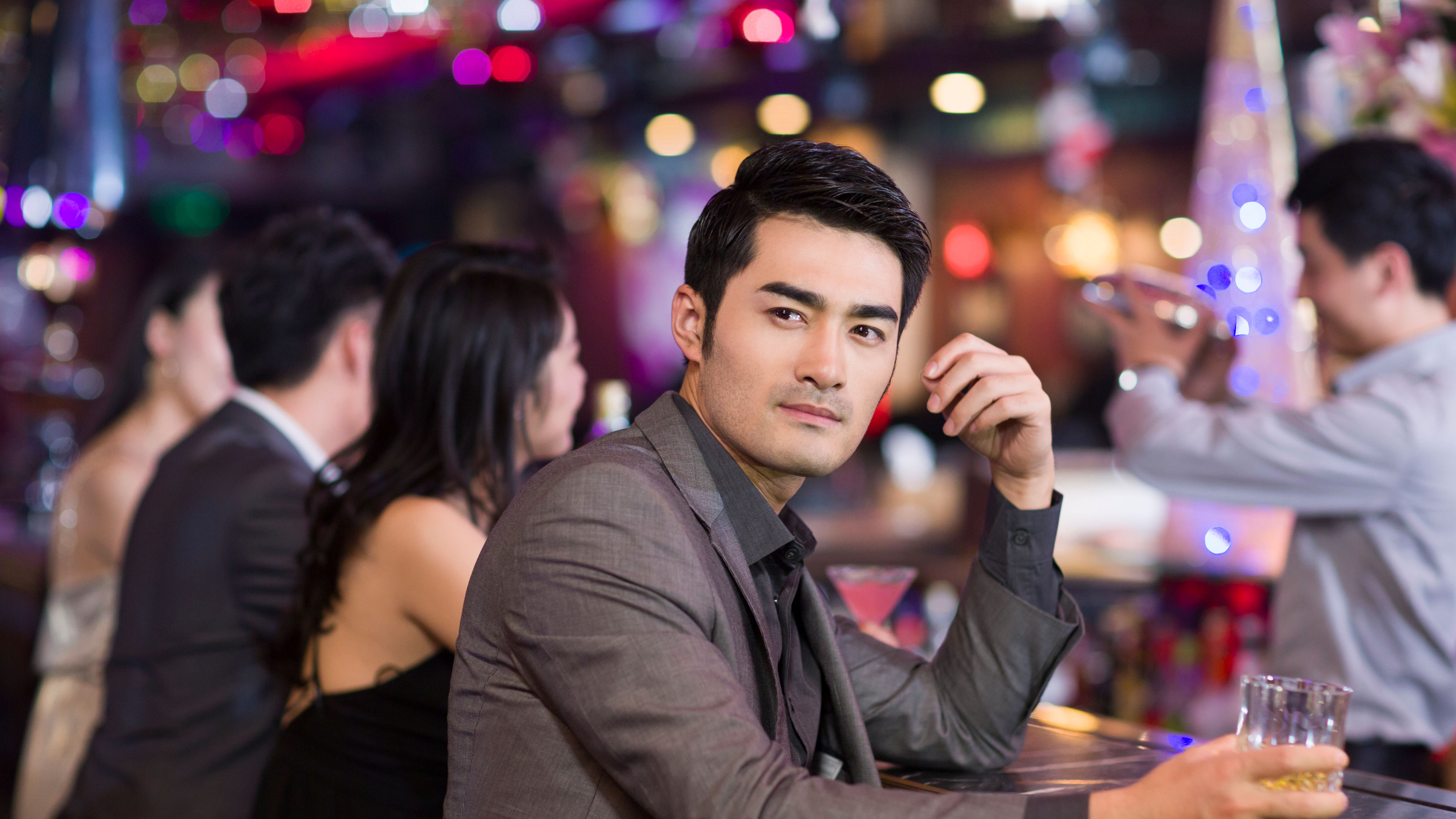 A young man enjoying a drink and having fun at a bar, surrounded by a lively atmosphere with vibrant lighting and energetic vibes. 