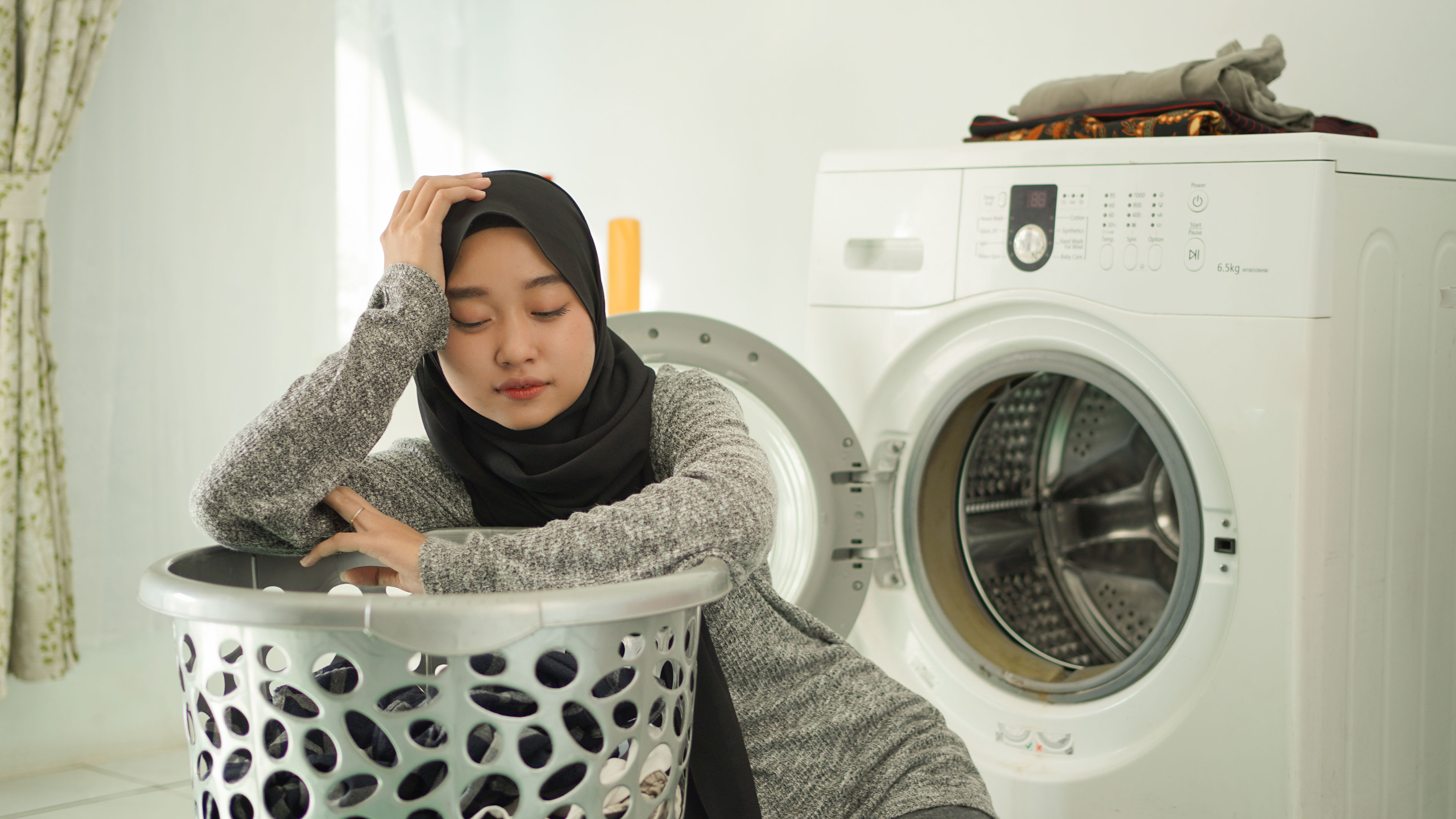 A young woman sits comfortably near a modern washing machine and organizing her laundry 